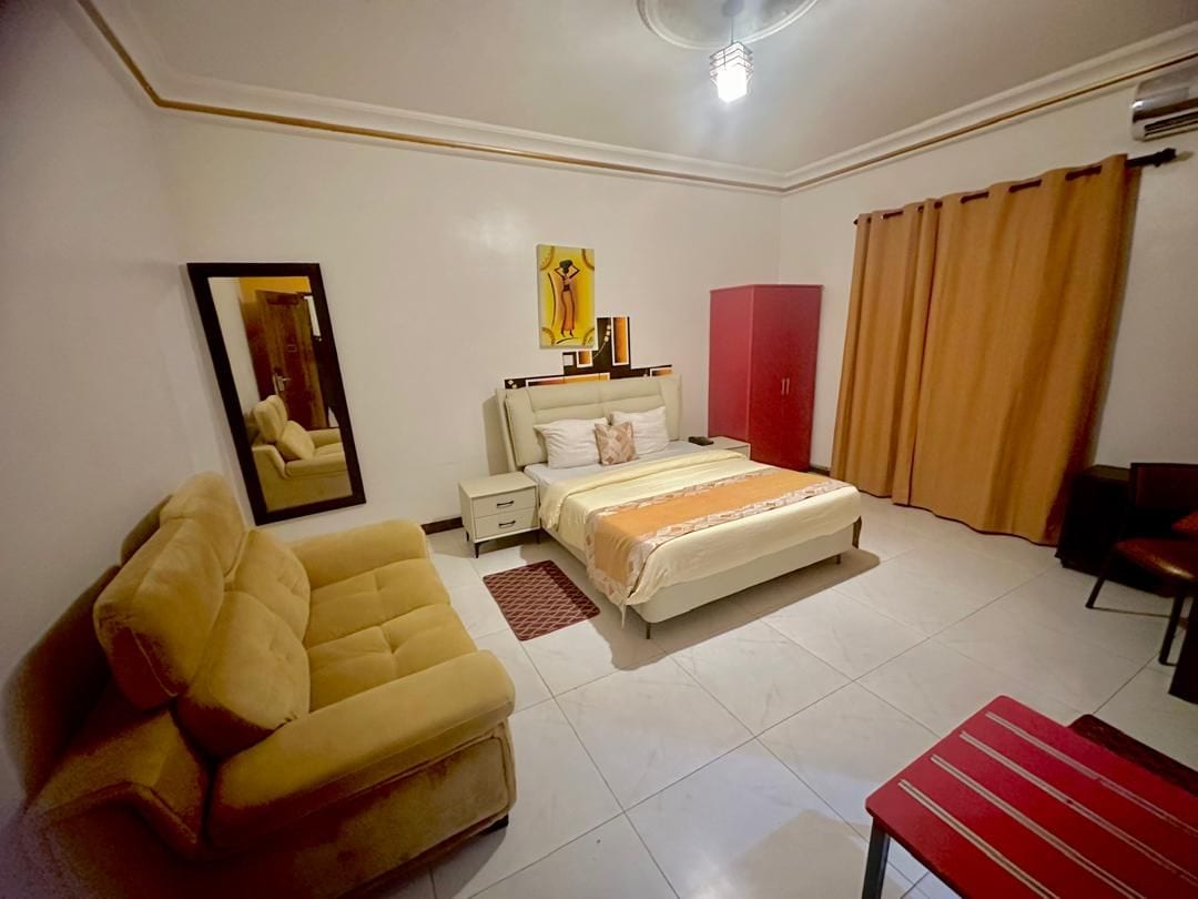 A hotel room with a bed, a sofa, a desk, a mirror, and a wardrobe.