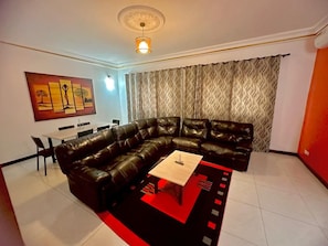 A living room with a sectional sofa, a coffee table, and a dining area with chairs.
