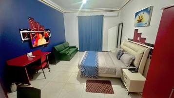 A bedroom with a bed, a desk, a chair, a wardrobe, and a television.