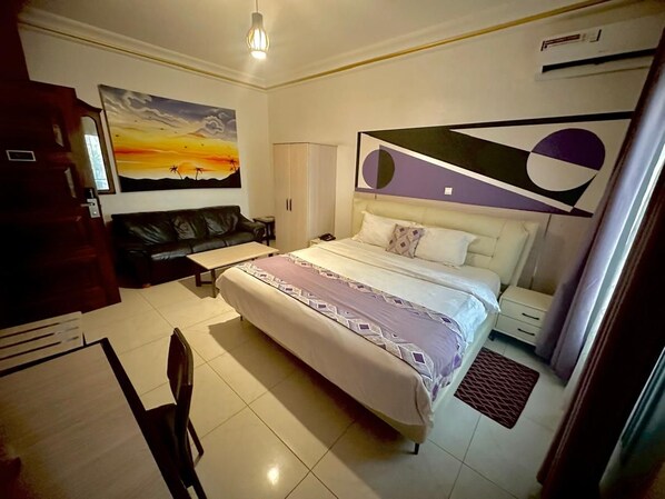 A hotel room with a bed, a desk, a chair, a painting on the wall, and a window.