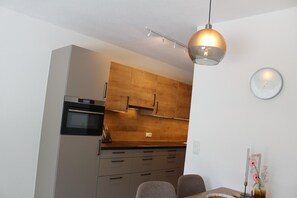 A modern kitchen with wooden cabinets, a built-in oven, and a dining area with a table and chairs. - Modern Apartment in the Tyrolean Mountains (Fliess)