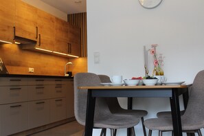 A modern kitchen with wooden cabinets, a dining table with chairs, and a wall clock. - Modern Apartment in the Tyrolean Mountains (Fliess)