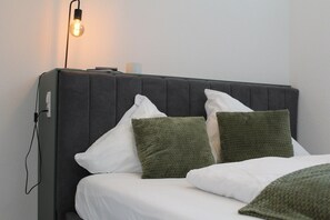A bed with white bedding and two pillows, one white and one green, against a wall with a light fixture. - Modern Apartment in the Tyrolean Mountains (Fliess)