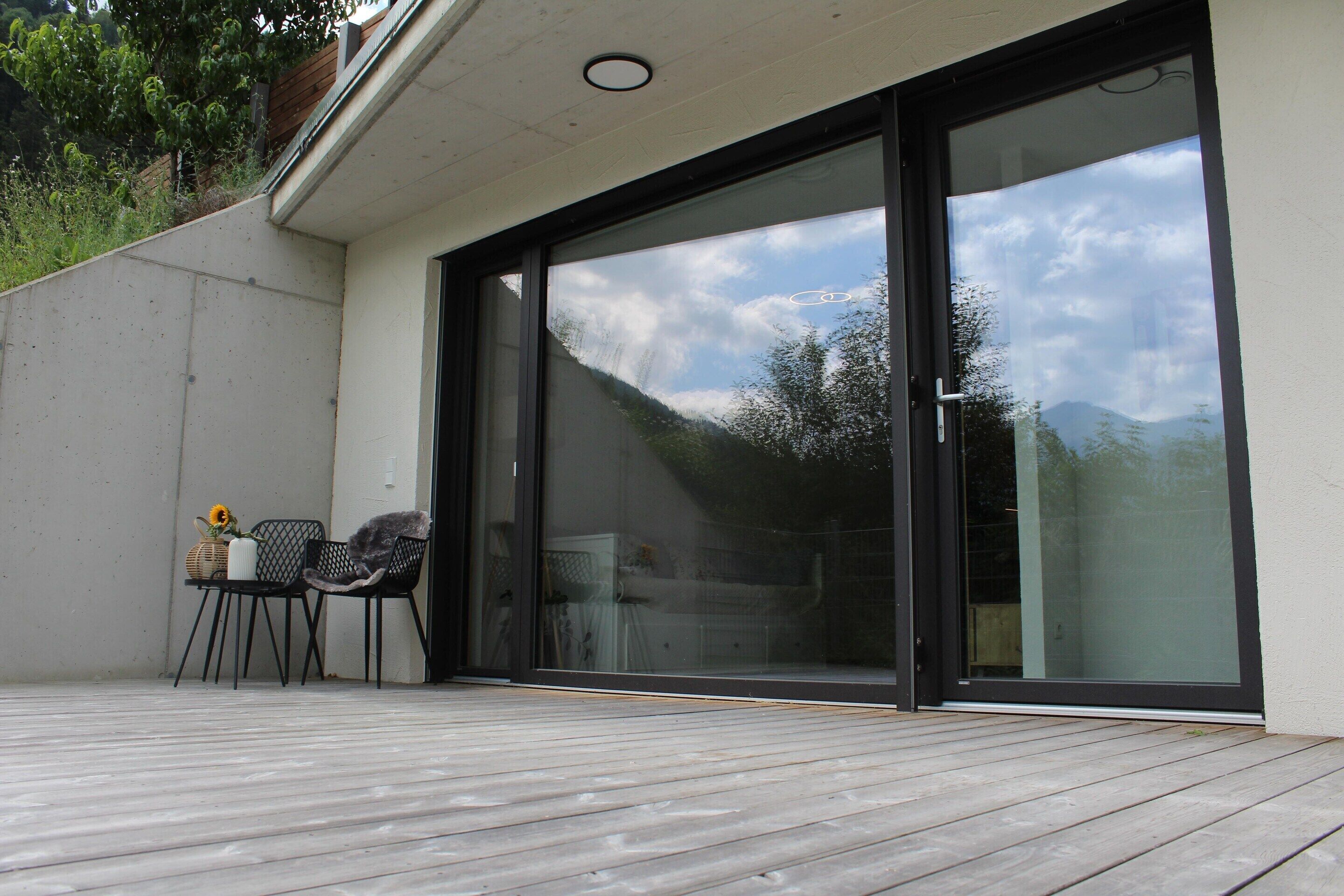 A deck with a table and chairs, a sliding glass door, and a view of a mountain landscape.