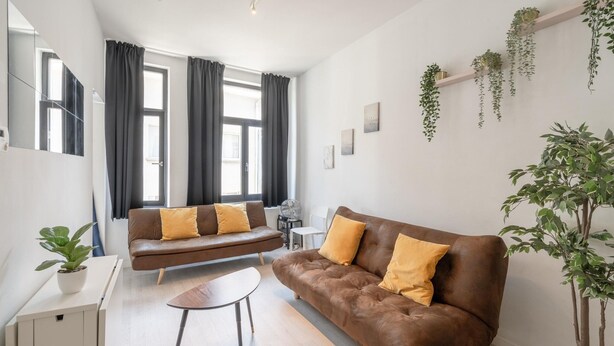 Una sala moderna con un sofá marrón, una mesita redonda y una planta en maceta.