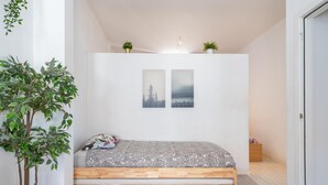 Un dormitorio con una cama de madera, dos cuadros en la pared, una planta pequeña en la pared y una planta en maceta junto a la cama.
