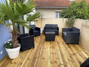 A patio with wicker furniture, a potted plant, and a wooden floor. - A cozy and modern family home (Suresnes)