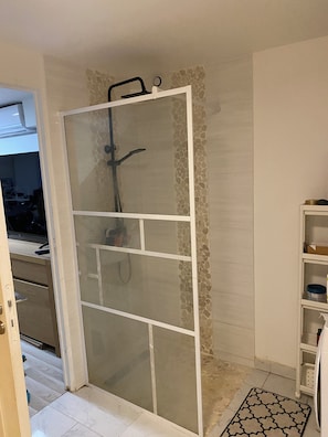Un bagno con cabina doccia, pavimento piastrellato e pensile bianco.
