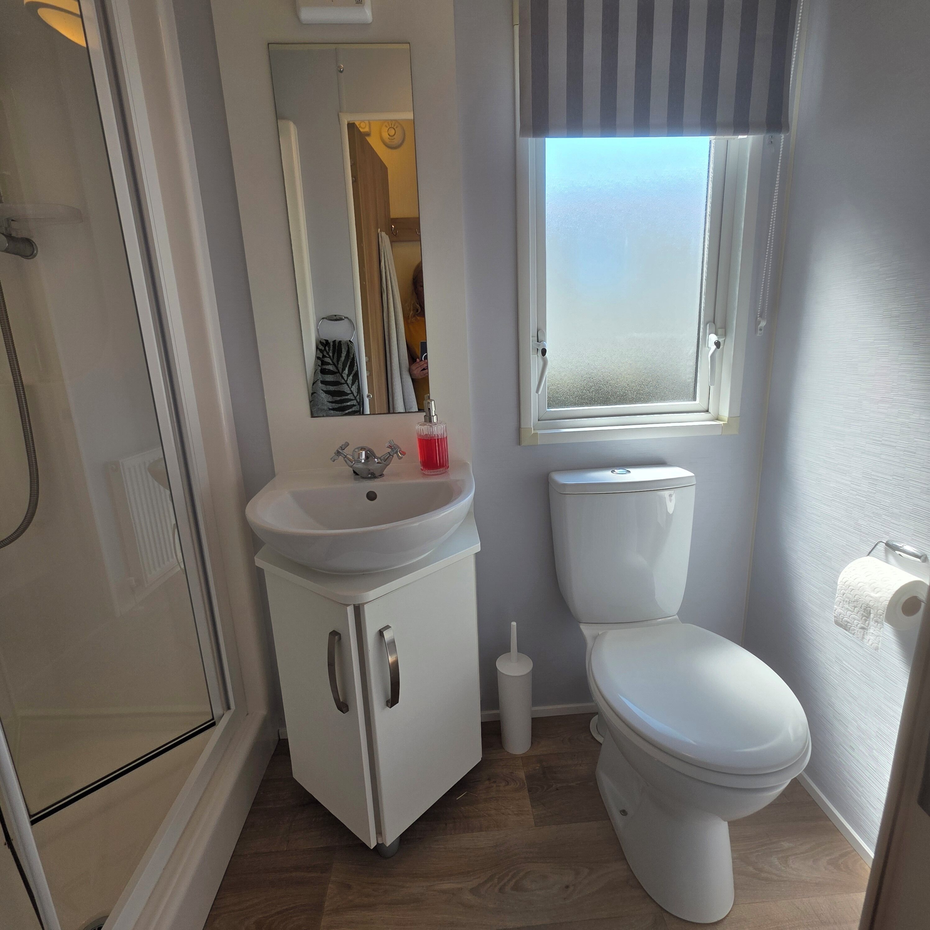 A bathroom with a shower, sink, toilet, and a window.
