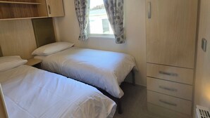 Quarto com duas camas, um guarda-roupa e uma janela com cortinas.