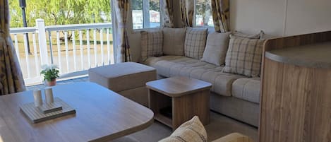 A modern RV interior with a sofa, two tables, and a mirror.