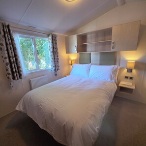A bedroom with a bed, bedside lamps, a window with curtains, and built-in storage. - Idyllic Holiday Park Home with Pool and Fishing Lakes.  Crantock, Cornwall (Crantock)