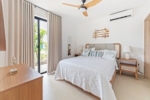 A hotel room with a bed, a desk, a ceiling fan, an air conditioning unit, and a view of the outdoors. - 1BR golf suites Apt In Punta Cana at Resort Style Residential w/Artificial Beach (Punta Cana)