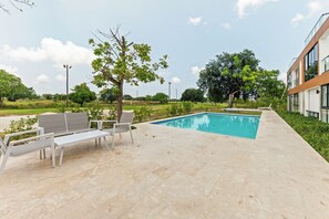 Une piscine avec des chaises longues et un arbre, le tout situé dans un espace extérieur aménagé.