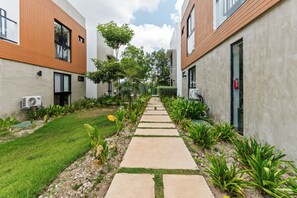 A pathway flanked by buildings with a garden and plants. - 1BR golf suites Apt In Punta Cana at Resort Style Residential w/Artificial Beach (Punta Cana)