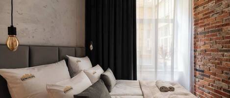 A hotel room with a bed, pillows, a blanket, a towel, a hanging light fixture, and a brick wall.