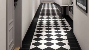 Un couloir avec un sol à carreaux noirs et blancs, des murs blancs et des tableaux encadrés accrochés aux murs.