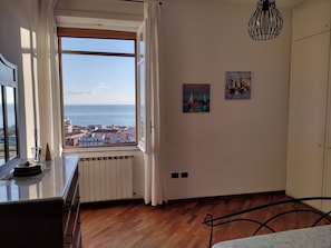 A room with a large window overlooking a cityscape, a radiator, a bed with a metal frame, and two wall-mounted paintings. - Mare in Vista Salerno - Amalfi Coast Rooftop (Salerno)