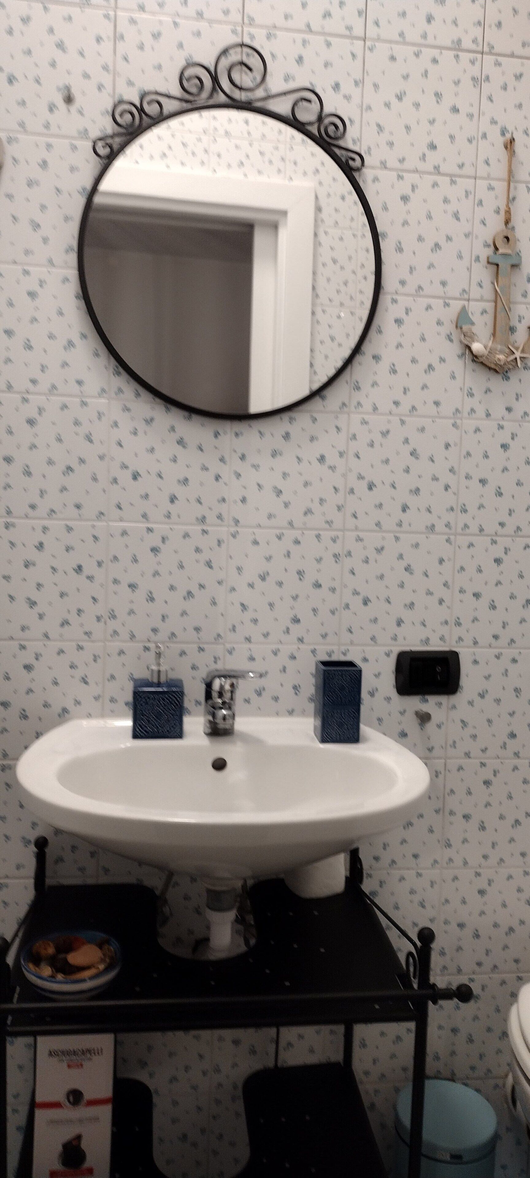 Ein Badezimmer mit einem weißen Waschbecken, einem runden Spiegel und einem blauen Handtuchhalter.
