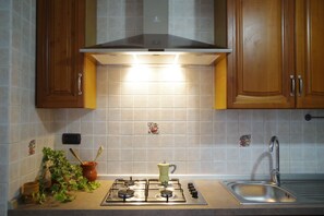 A kitchen with a gas stove, a range hood, wooden cabinets, and a tiled backsplash. - Mare in Vista Salerno - Amalfi Coast Rooftop (Salerno)