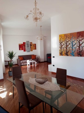 A modern living room with a glass dining table, a sofa, a coffee table, and a chandelier. - Mare in Vista Salerno - Amalfi Coast Rooftop (Salerno)