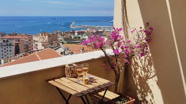En balkon med et bord, to glas og en potteplante med lyserøde blomster.