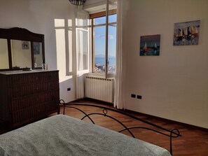 Quarto com cama, cômoda, janela com vista e duas pinturas na parede.