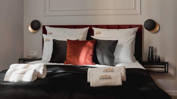 A neatly made bed with a red headboard, white and black pillows, and a pair of towels with a logo. - Charm & Chic Studio 21.1 | Main Old Town & Planty (Kraków)
