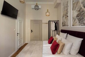 Ein Hotelzimmer mit einem Bett, einem an der Wand montierten Fernseher, einem Kleiderständer und Bildern an der Wand.