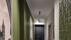 Un pasillo con piso a cuadros, paredes verdes y cuadros en la pared izquierda.