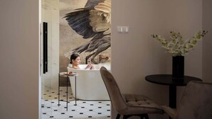 Ein modernes Badezimmer mit einer großen Wandmalerei, einer Badewanne, einem kleinen runden Tisch und einem Blumenstrauß.