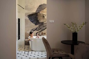 A modern bathroom with a large mural, a bathtub, a small round table, and a vase of flowers. - Charm & Chic Studio 26.1 | Jacuzzi | Main Old Town (Kraków)