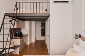 A compact studio apartment with a loft bed, kitchenette, and a view of a cityscape. - Charm & Chic Studio 21.3 | Main Old Town & Planty (Kraków)