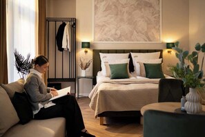Et hotelværelse med seng, siddeplads, et natbord og et stort billede på væggen.