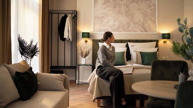A hotel room with a bed, a sitting area with a table, a coat rack, and a wall-mounted artwork. - Charm & Chic Studio 24.1 | Main Old Town & Planty (Kraków)