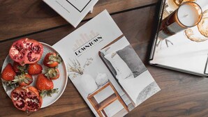 Un magazine dont la couverture représente un paysage urbain, une assiette de fraises et de grenades, et une bougie posée sur une table en bois.
