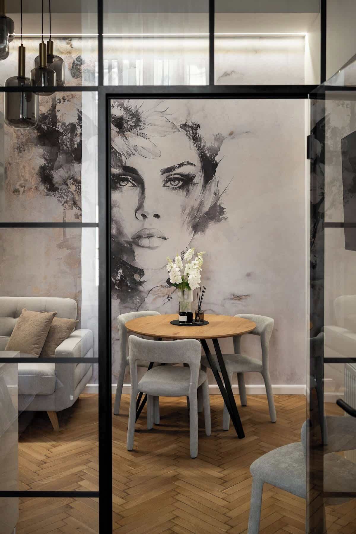 Ein modernes Interieur mit einem runden Esstisch, grau gepolsterten Stühlen und einem großen, abstrakten Gemälde an der Wand.
