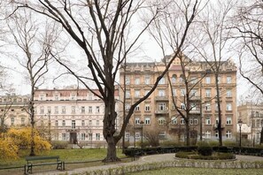 A park with a large tree and a bench, a building with multiple windows in the background. - Charm & Chic Studio 21.2 | Main Old Town & Planty (Kraków)