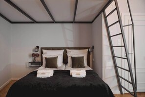 A hotel room with a bed, a nightstand, a vase with flowers, and a ladder against the wall. - Charm & Chic Studio 21.2 | Main Old Town & Planty (Kraków)