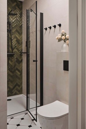 A modern bathroom with a glass shower enclosure, a toilet, and a decorative vase with flowers. - Charm & Chic Studio 21.2 | Main Old Town & Planty (Kraków)