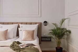 Ein Schlafzimmer mit Bett, Kissen, Nachttisch, Lampe und einer Zimmerpflanze.