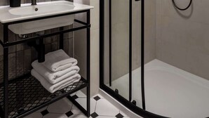 Ein modernes Badezimmer mit einer gläsernen Duschkabine, einem weißen Waschbecken mit schwarzem Wasserhahn und einem Spiegel mit beleuchtetem Rahmen.