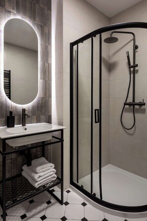 Ein modernes Badezimmer mit einer gläsernen Duschkabine, einem weißen Waschbecken mit schwarzem Wasserhahn und einem Spiegel mit beleuchtetem Rahmen.