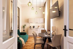 Ein modernes Wohnzimmer mit einem grünen Sofa, einem Esstisch mit Stühlen und einer Küche im Hintergrund.