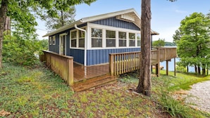 Une petite cabane dotée d’une terrasse, entourée d’arbres et bordée par un plan d’eau.