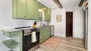 Une cuisine avec des meubles de rangement verts, un four en acier inoxydable, un évier et un plancher en bois.