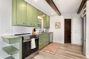 A kitchen with green cabinets, a stainless steel oven, a sink, and a wooden floor.