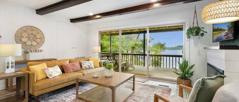 A spacious living room with a large sofa, coffee table, and a view of a lake through the sliding glass doors.