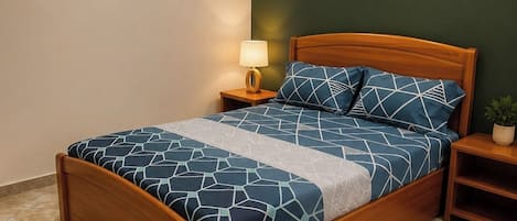 A bedroom with a wooden bed, a nightstand with a lamp, and a wall-mounted light fixture.