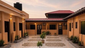 A courtyard with a tiled floor, potted plants, and a building with a red roof.